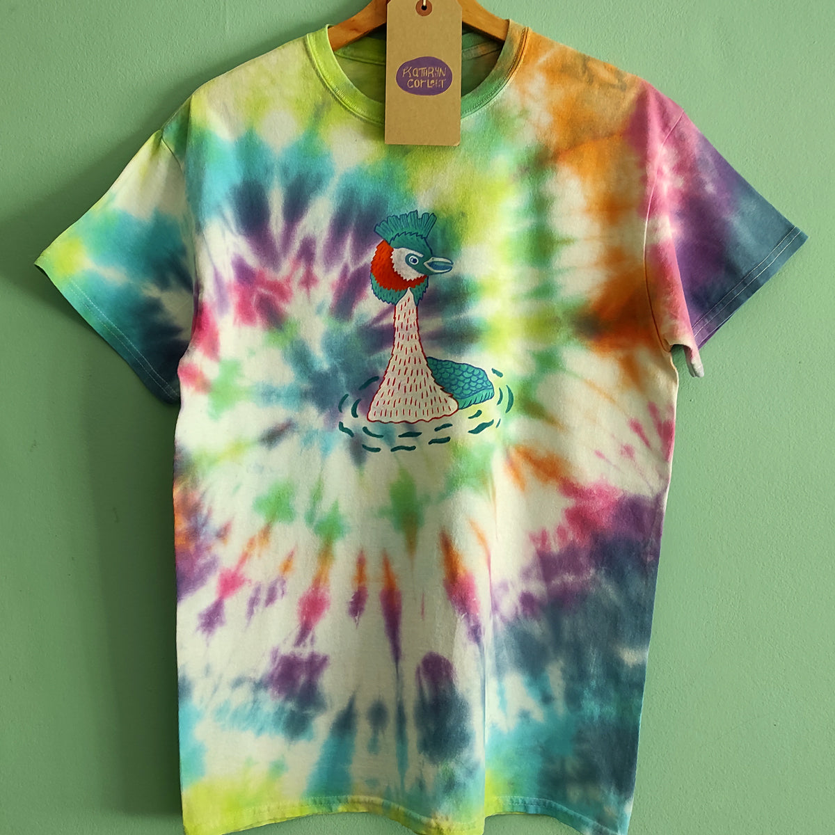 Colourful tie dye t-shirt on green background with a hand illustrated Great Crested Grebe in the centre