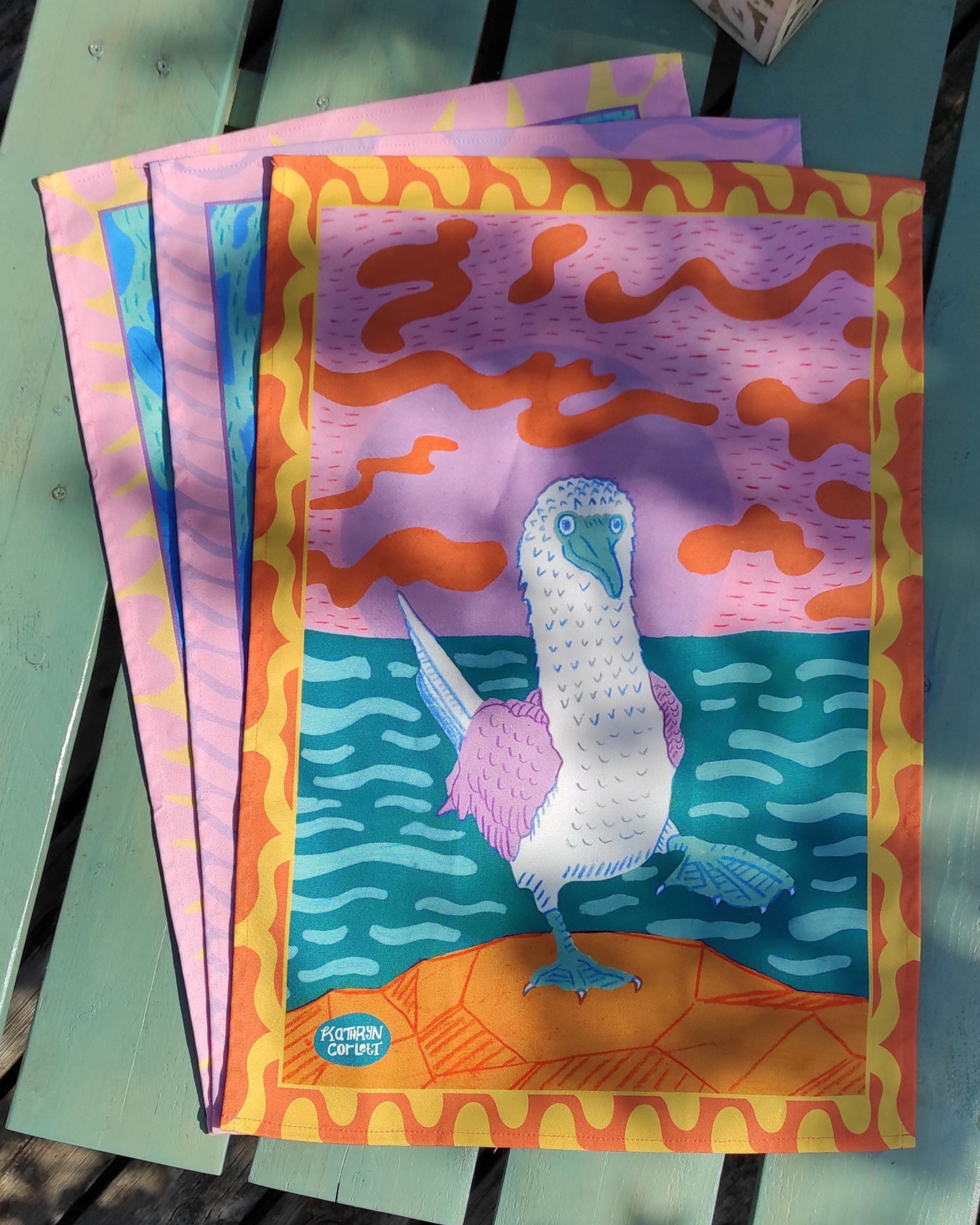A colourful tea towel with a Blue Footed Booby design on a green surface