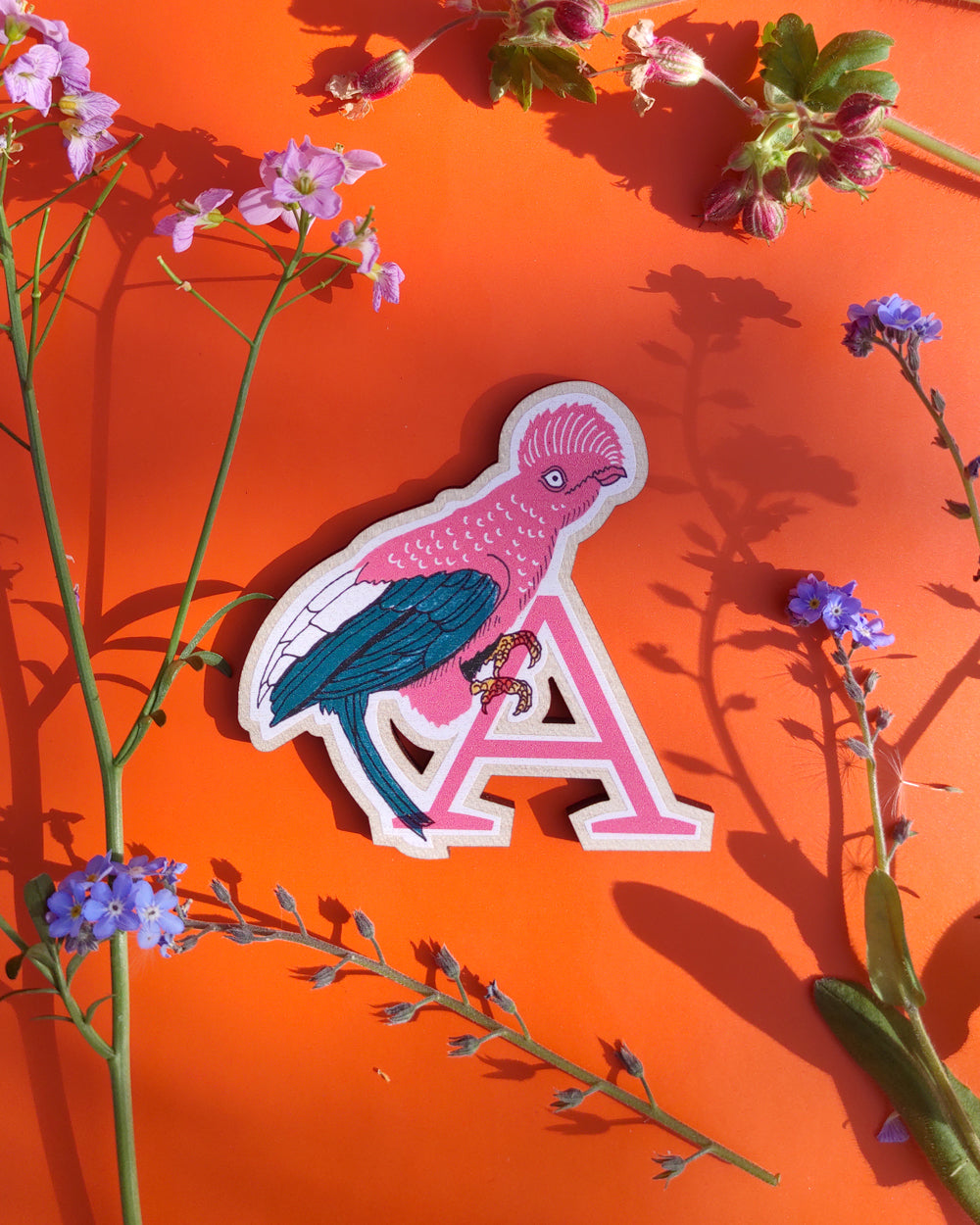 Letter 'A' wood cut with a bird design on an orange background with flowers