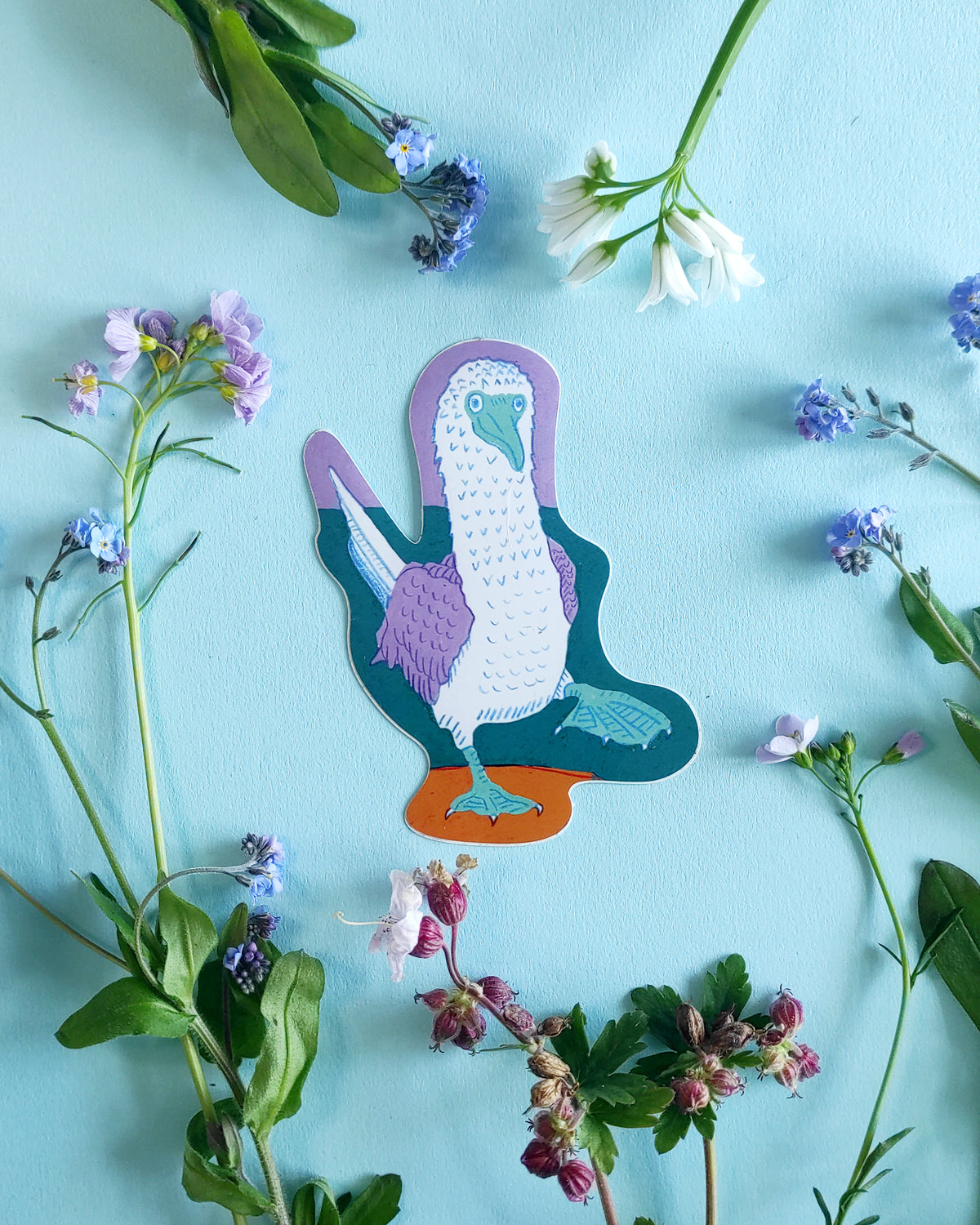 Blue-footed booby sticker on a blue background with green leaves and flowers