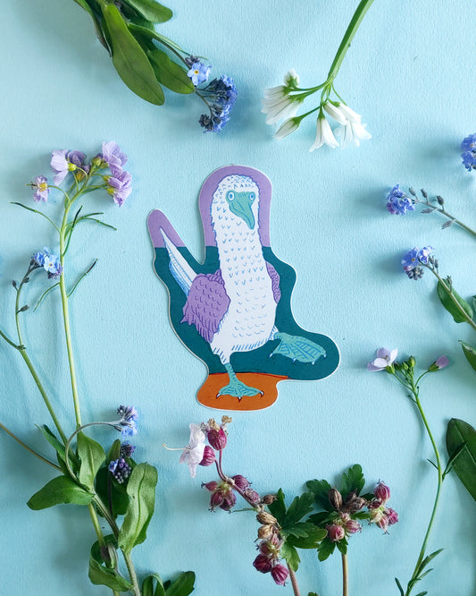 Blue-footed booby sticker on a blue background with green leaves and flowers