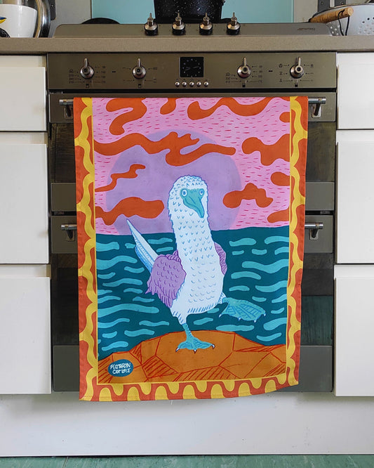 A colourful tea towel with a Blue Footed Booby design hanging in front of an oven