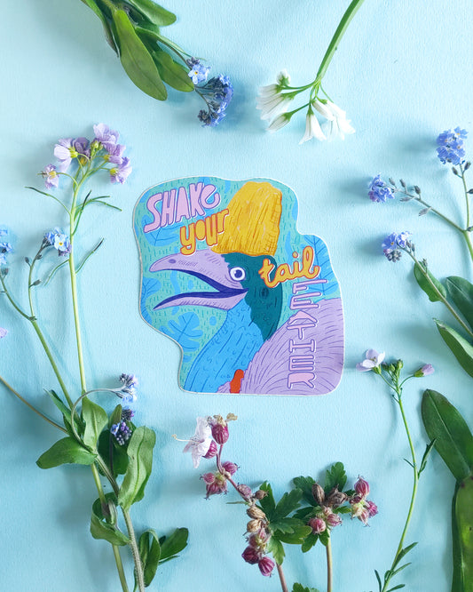 Colorful sticker with a bird design and text 'Shake your tail' surrounded by flowers on a light blue background