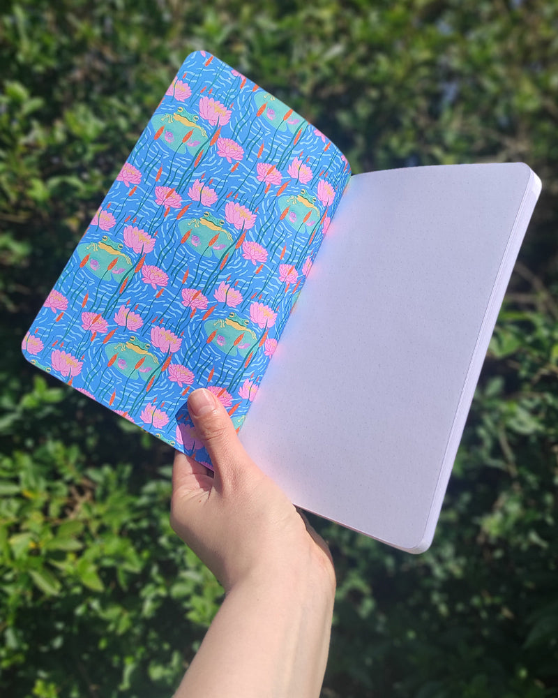Hand holding a colorful notebook with a pattern against a green leafy background