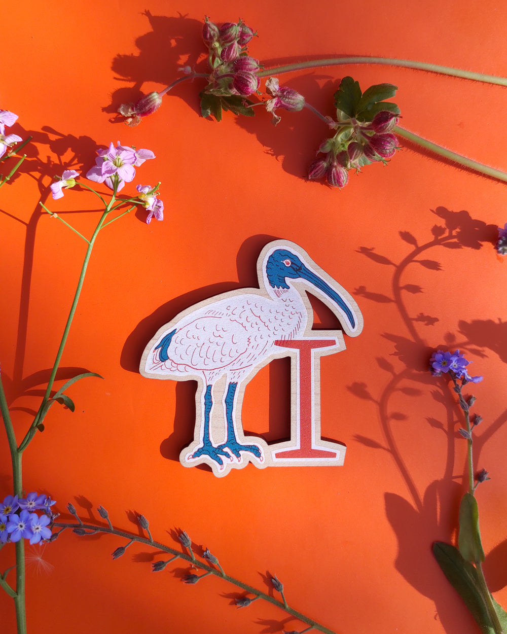 Decorative letter 'I' shaped like an ibis on an orange background with flowers.