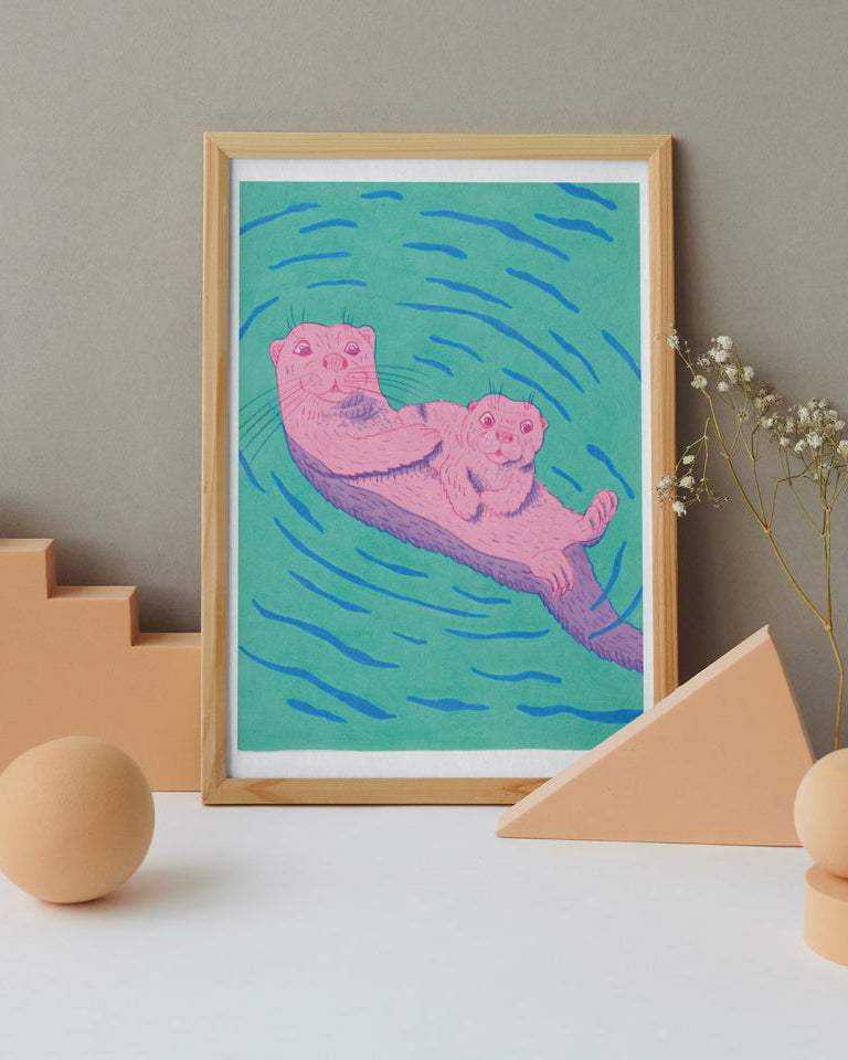 Framed artwork of an otter Mum and Pup floating in water with geometric shapes and flowers on a neutral background