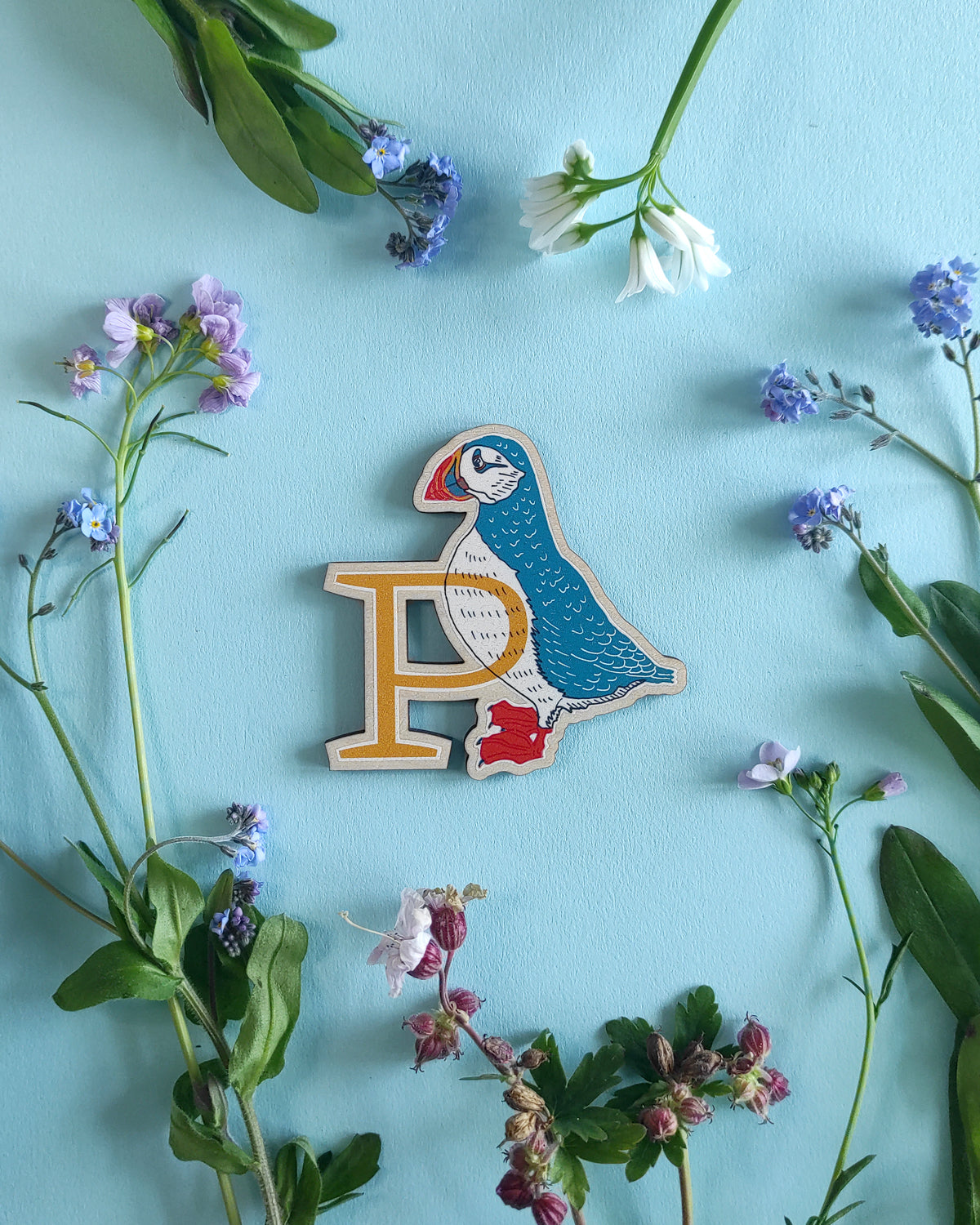 Wooden letter 'P' with a puffin design on a blue background with flowers and leaves.