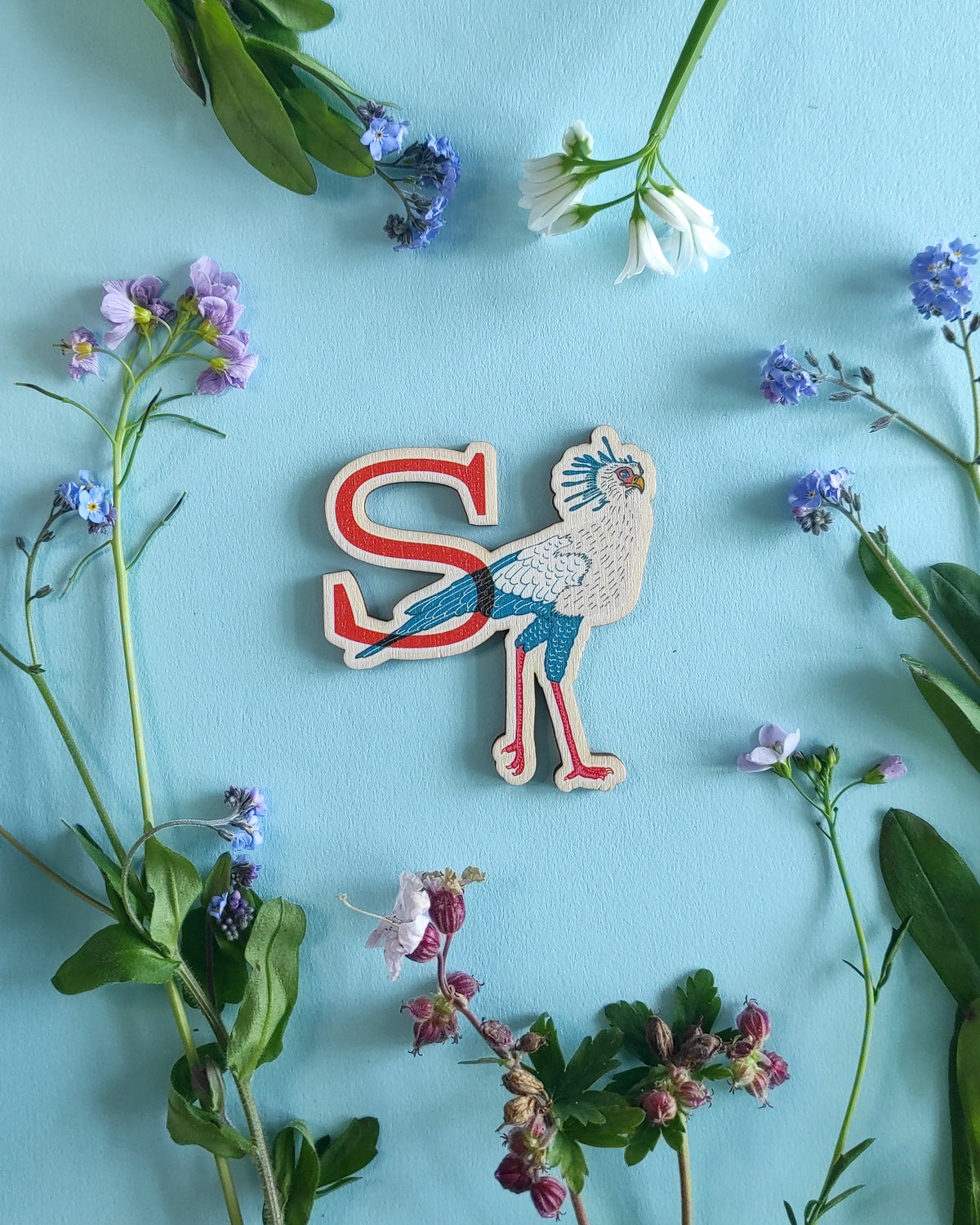 Wooden letter 'S' with a secretary bird design on a blue background with flowers and leaves.