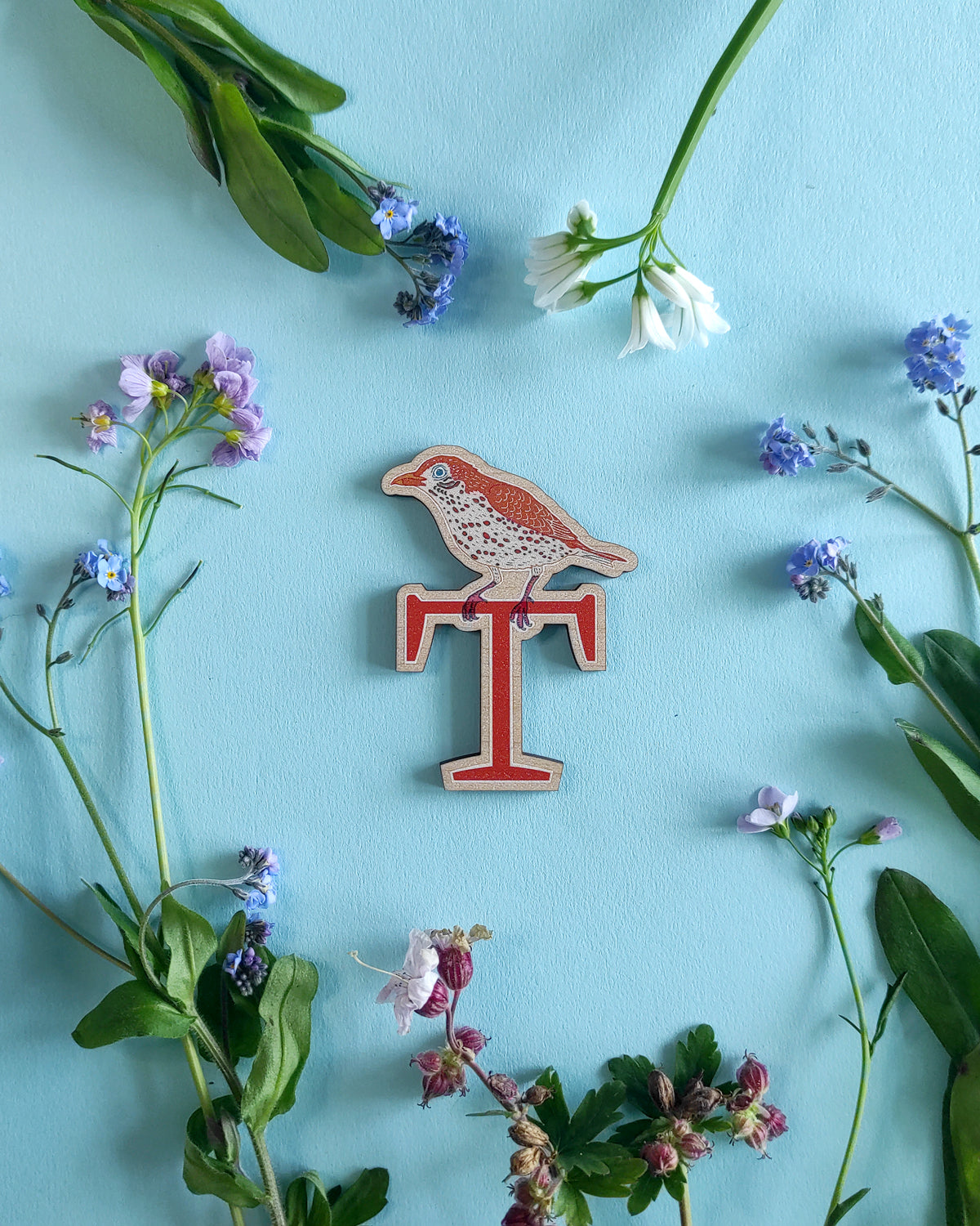 Wooden letter 'T' with a thrush design on a blue background with flowers and leaves.