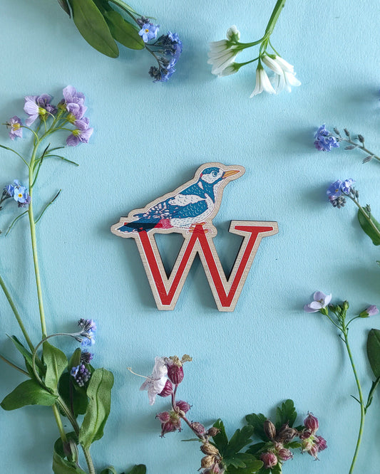 Wooden letter 'W' with a woodpecker bird design on a blue background with flowers and leaves.